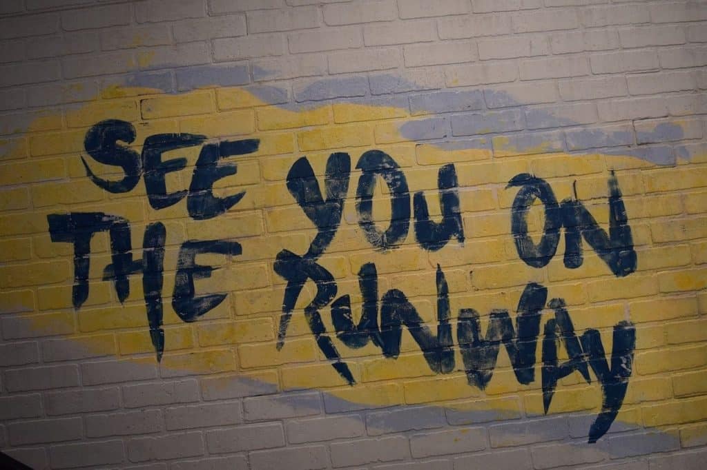 SeeYou-see-pixabay-weksart-you-on-the-runway-2939863_1280-170921 Eine Backsteinwand mit der Aufschrift "SEE YOU ON THE RUNWAY" in großen, blauen, unregelmäßigen Buchstaben auf gelbem Hintergrund verleiht jeder Veranstaltungstechnik ein besonderes Flair.