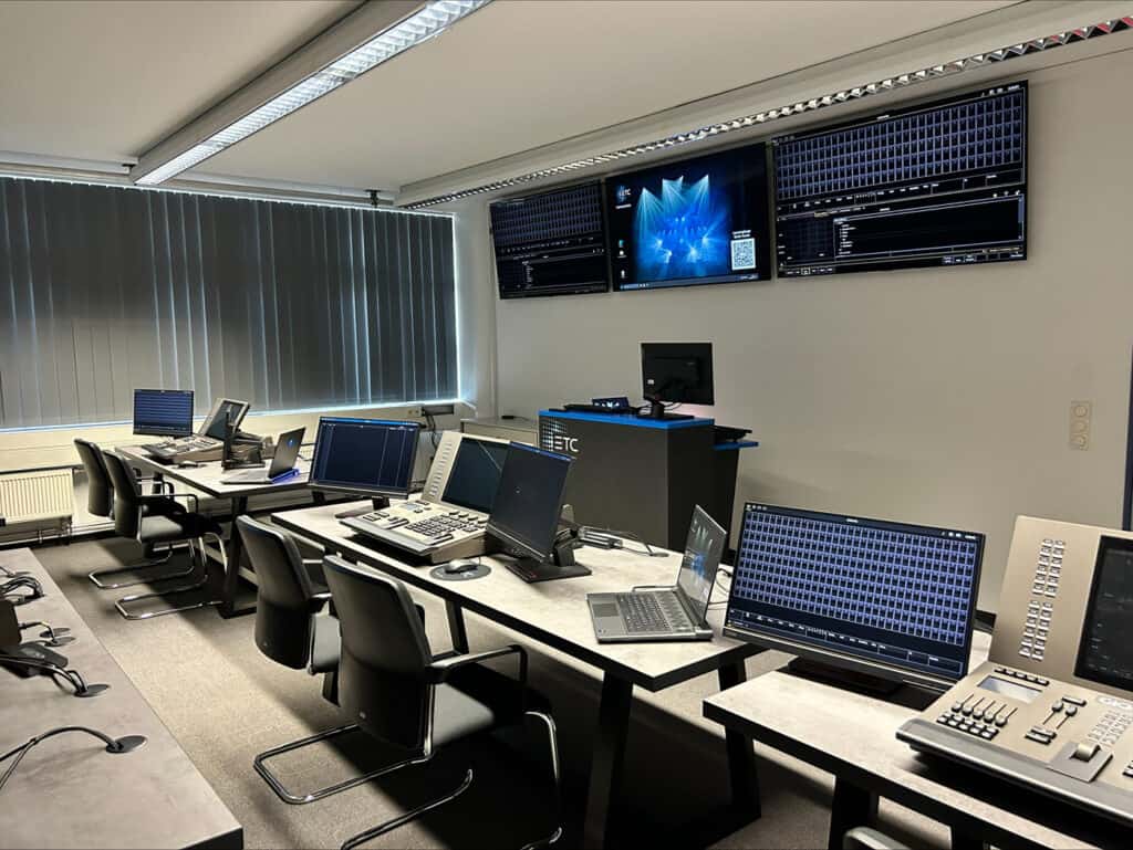 Ein moderner Kontrollraum mit mehreren Schreibtischen, Laptops, Konsolen und großen Monitoren an der Wand, die technische Daten und Grafiken anzeigen.