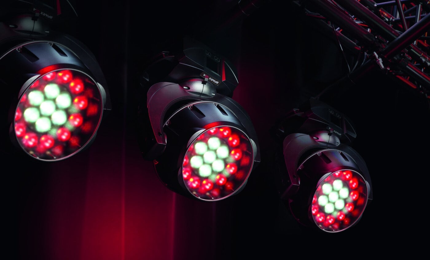 Drei Bühnenscheinwerfer mit einer Mischung aus roten und weißen LED-Lampen sind auf einem Metallrahmen montiert und leuchten nach unten vor einem dunklen Hintergrund.