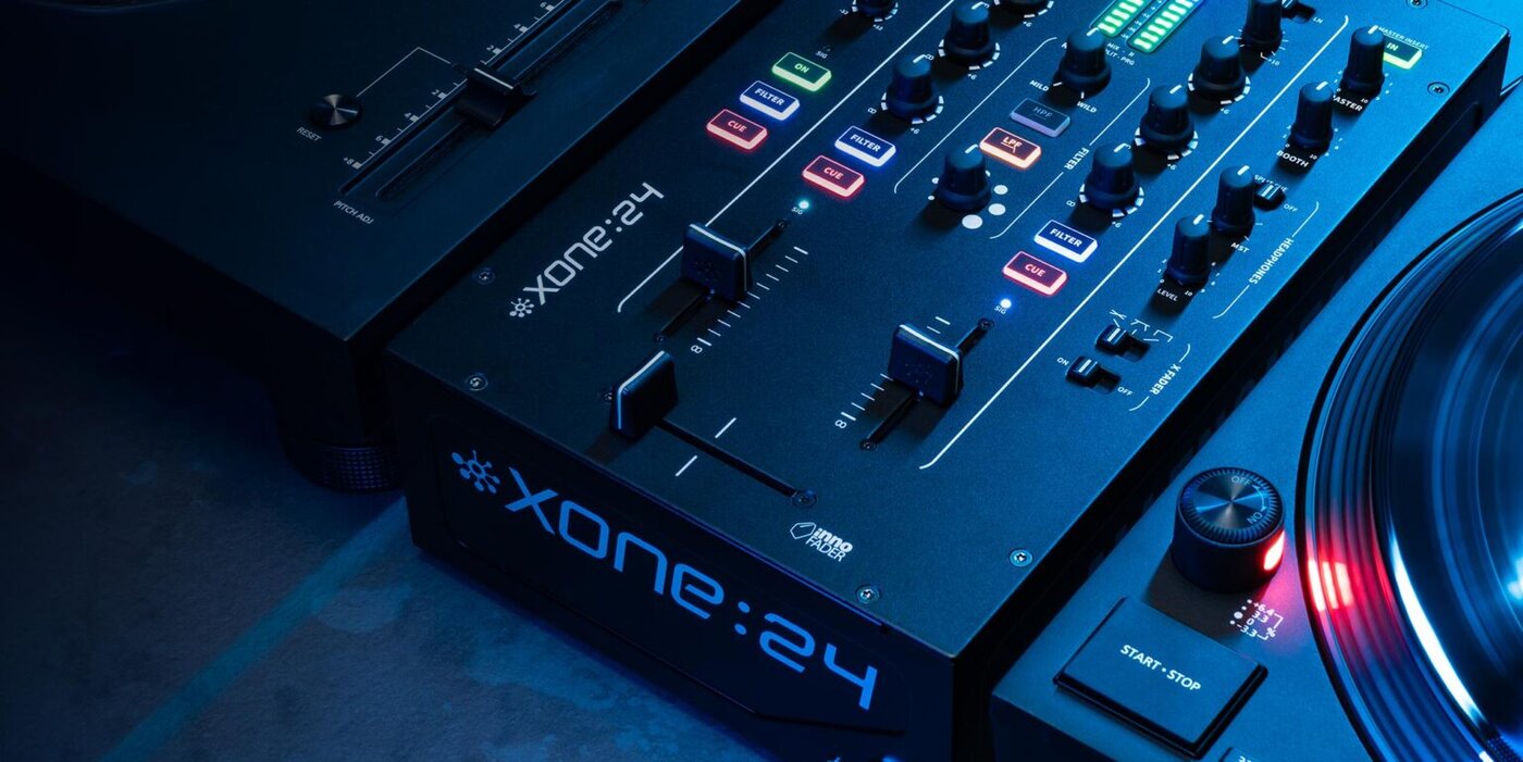 Nahaufnahme eines Xone:24-Audiomischers mit beleuchteten Tasten und Schiebereglern, daneben ein Plattenspieler mit leuchtender Einschalttaste, alles blau beleuchtet.