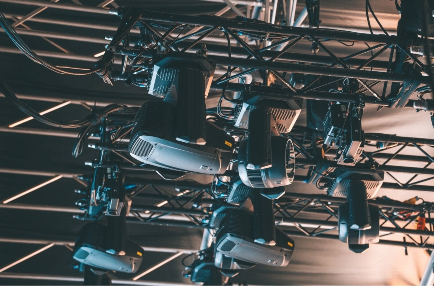 Mehrere Bühnenscheinwerfer sind an einer Metalltraverse montiert, deren Kabel sichtbar sind. Sie gehören wahrscheinlich zu einer professionellen Beleuchtungsanlage für eine Veranstaltung oder einen Auftritt.