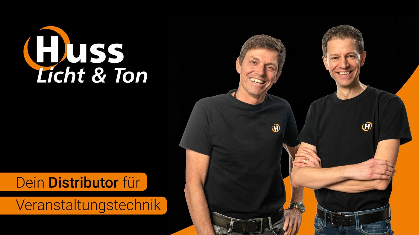 Zwei Männer in schwarzen Huss Licht & Ton-T-Shirts stehen lächelnd da. Links: Firmenlogo. Unten links: orangefarbener Kasten mit deutschem Text über den Vertrieb von Veranstaltungstechnik auf der Huss Expo 2026.