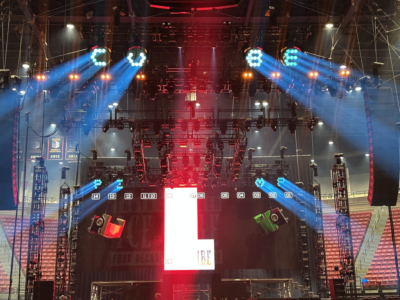 Eine Konzertbühne mit hellen Lichtern, Metalltraversen und einem großen vertikalen LED-Bildschirm, auf dem ein rot-weißes "L" zu sehen ist, in einer Indoor-Arena.