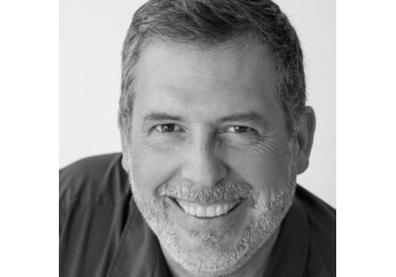 op25_stefan_wolf_profil.f0b9b823 Schwarz-Weiß-Kopffoto eines Mannes mittleren Alters mit kurzen Haaren, Bart und einem freundlichen Lächeln, der in die Kamera schaut, vor einem schlichten Hintergrund.