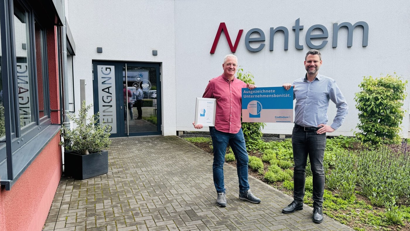 Aventem-mit-CrefoZert-ausgezeichnet-scaled Zwei Männer stehen vor einem Gebäude neben einem Schild mit der Aufschrift „Aventem“. Der eine hält eine gerahmte Urkunde in der Hand, der andere ein Schild, auf dem „Corporate Health Excellence“ steht.