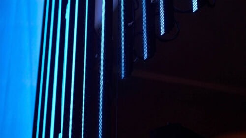 Vertikale blaue LED-Lichtleisten sind vor einem dunklen Hintergrund angebracht, wobei oben rechts einige Kabel und Befestigungen zu sehen sind.