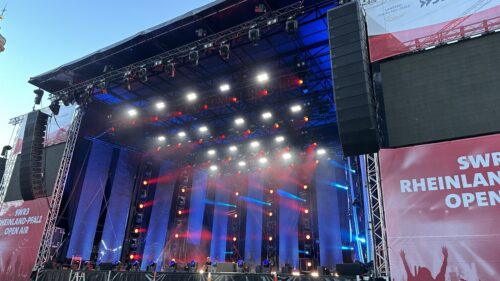 Große Open-Air-Konzertbühne mit roter und blauer Beleuchtung, mehreren Bildschirmen und Bannern mit der Aufschrift „SWR3 Rheinland-Pfalz Open Air“ bei Tageslicht.
